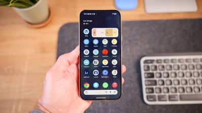 Mano sujetando un Google Pixel 11 Pro mostrando el menú de aplicaciones de Android 17 sobre un escritorio.