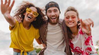 Tres jóvenes sonrientes abrazados posando para un selfie al aire libre.