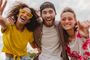 Tres jóvenes sonrientes abrazados posando para un selfie al aire libre.