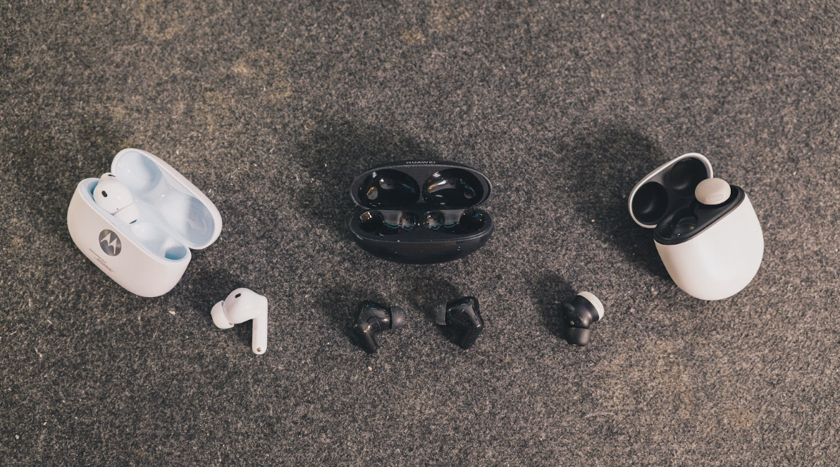 Tres pares de auriculares inalámbricos de diferentes marcas junto a sus estuches sobre una superficie rugosa.