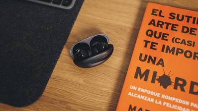 Estuche de carga abierto de los auriculares Huawei FreeBuds Neo sobre una mesa de madera junto a un libro naranja.