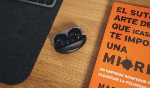 Estuche de carga abierto de los auriculares Huawei FreeBuds Neo sobre una mesa de madera junto a un libro naranja.