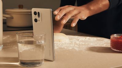 Mano de una persona controlando mediante gestos en el aire un smartphone OPPO Find X5 Pro de color blanco apoyado en una encimera de cocina con harina.