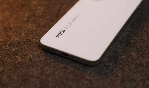 Detalle de la parte inferior trasera de un smartphone POCO en color blanco sobre una superficie rugosa.