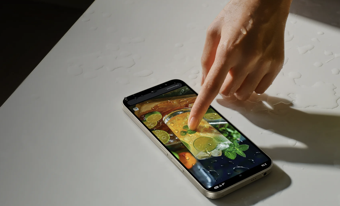 Dedo pulsando la pantalla de un Redmi 17 5G sobre una superficie blanca con gotas de agua.
