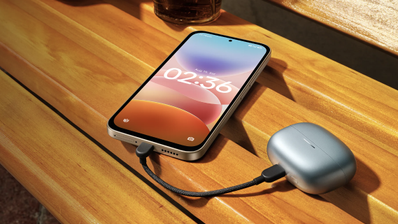 Teléfono Redmi 17 5G conectado por cable USB-C al estuche de unos auriculares inalámbricos sobre una mesa de madera.