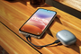 Teléfono Redmi 17 5G conectado por cable USB-C al estuche de unos auriculares inalámbricos sobre una mesa de madera.