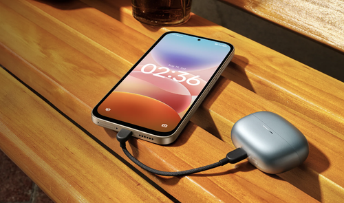Teléfono Redmi 17 5G conectado por cable USB-C al estuche de unos auriculares inalámbricos sobre una mesa de madera.