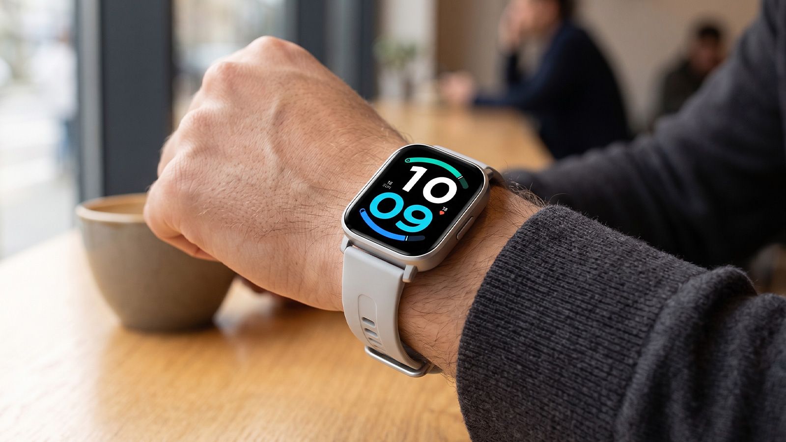Reloj inteligente Redmi Watch 6 Active con esfera digital en la muñeca de un usuario en una cafetería.
