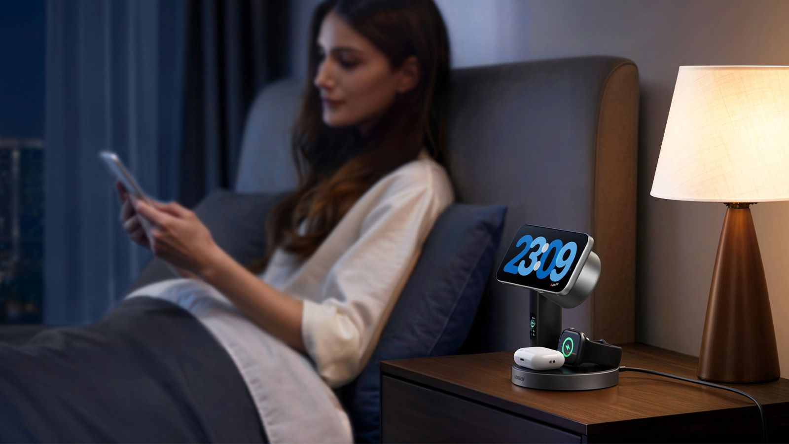 Estación de carga inalámbrica UGREEN MagFlow Pro 3 en 1 en una mesita de noche junto a una persona en la cama.
