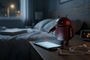 Figura metálica del robot de Android manipulando la pantalla encendida de un teléfono móvil sobre una mesita de noche en un dormitorio oscuro.