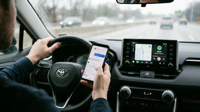 Conductor interactuando con un smartphone y la pantalla de Android Auto en el salpicadero de un coche.