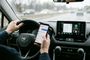 Conductor interactuando con un smartphone y la pantalla de Android Auto en el salpicadero de un coche.