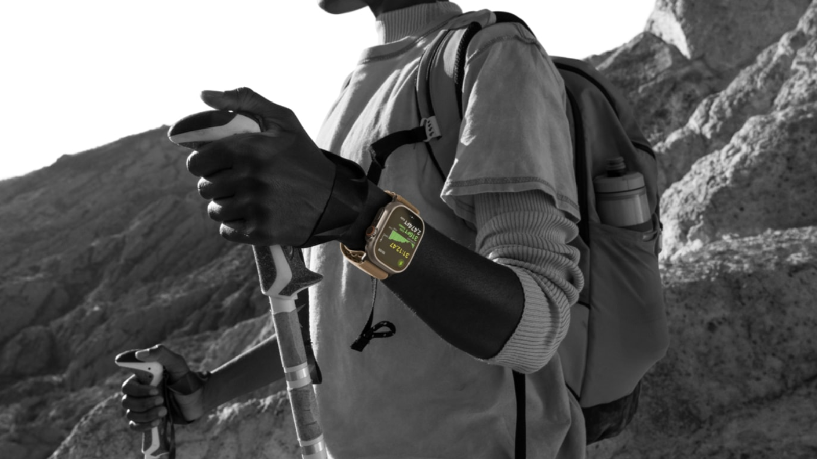 Primer plano de una persona haciendo senderismo con un Apple Watch Ultra 4 en la muñeca mientras sujeta bastones de montaña.