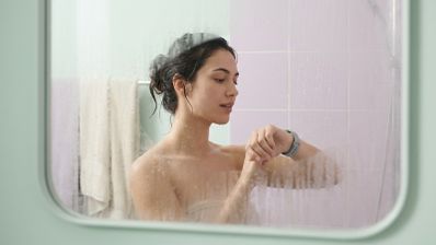 Mujer consultando una pulsera inteligente mientras se ducha frente a un espejo empañado.