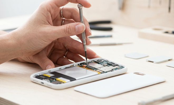 Primer plano de un técnico utilizando un destornillador de precisión sobre los circuitos internos de un teléfono móvil blanco desmontado.