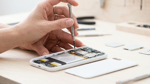 Primer plano de un técnico utilizando un destornillador de precisión sobre los circuitos internos de un teléfono móvil blanco desmontado.