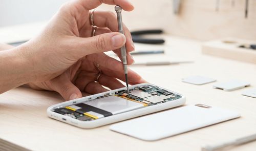 Primer plano de un técnico utilizando un destornillador de precisión sobre los circuitos internos de un teléfono móvil blanco desmontado.