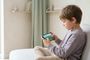 Niño sentado de perfil en un sofá utilizando un teléfono móvil en posición horizontal para jugar a un videojuego.