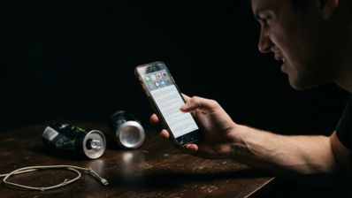 Persona con expresión de frustración mirando la pantalla de un teléfono móvil en una habitación oscura.