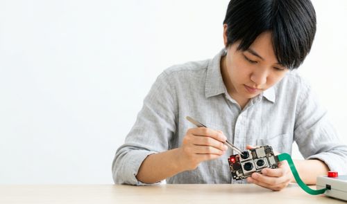 Técnico manipulando con pinzas un módulo de cámara de un dispositivo electrónico sobre una mesa de trabajo.
