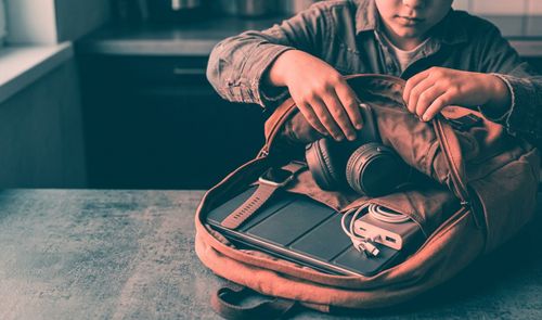 Niño metiendo en su maleta diferentes dispositivos para el colegio