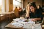 Mujer preocupada revisando documentos y mapas en una cafetería.