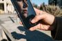 Primer plano de una persona sujetando un smartphone mientras la pantalla muestra un icono de reconocimiento facial sobre el reflejo de su rostro.
