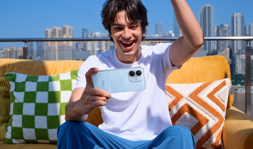 Joven sentado en una terraza sosteniendo en horizontal un REDMI Note 17 Pro 5G mientras celebra una partida.