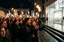 Multitud de personas protestando con antorchas encendidas y carteles frente a una tienda Apple Store iluminada de noche.