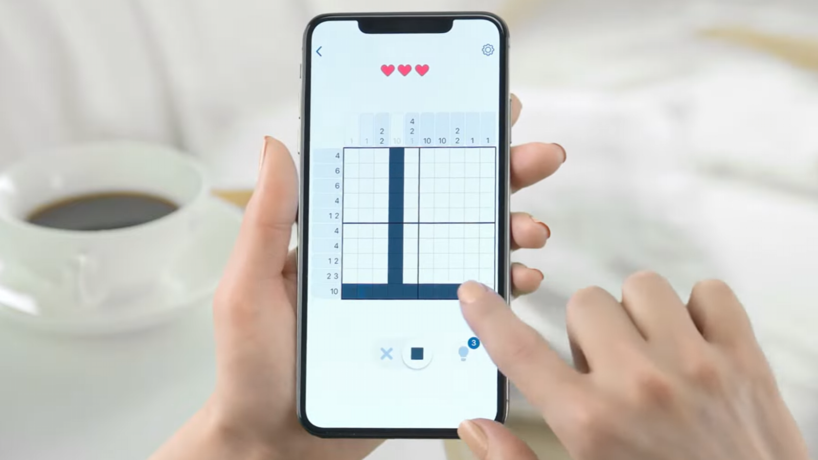 Persona jugando a un nonograma en un smartphone sobre una mesa con una taza de café.