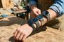 Persona con cuatro smartwatches y pulseras de actividad diferentes colocados en el brazo sobre una mesa de madera.