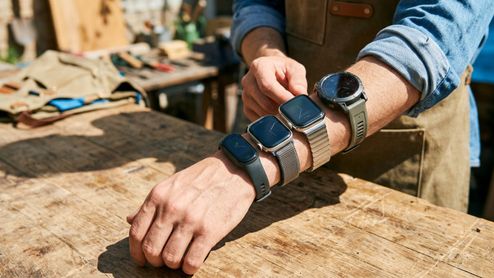 Persona con cuatro smartwatches y pulseras de actividad diferentes colocados en el brazo sobre una mesa de madera.