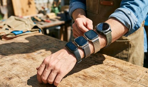 Persona con cuatro smartwatches y pulseras de actividad diferentes colocados en el brazo sobre una mesa de madera.