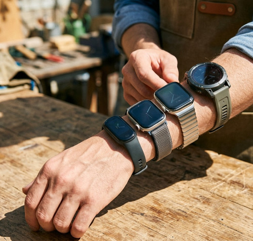 Persona con cuatro smartwatches y pulseras de actividad diferentes colocados en el brazo sobre una mesa de madera.