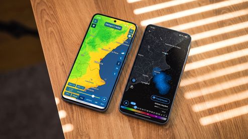 Dos teléfonos móviles sobre una mesa de madera mostrando mapas meteorológicos de la Comunidad Valenciana en sus pantallas.