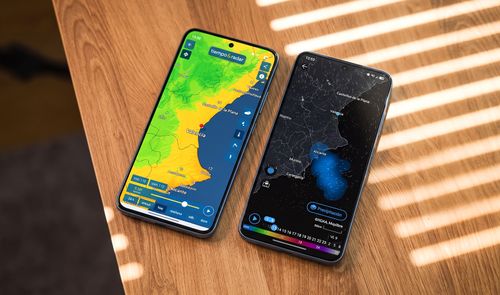 Dos teléfonos móviles sobre una mesa de madera mostrando mapas meteorológicos de la Comunidad Valenciana en sus pantallas.