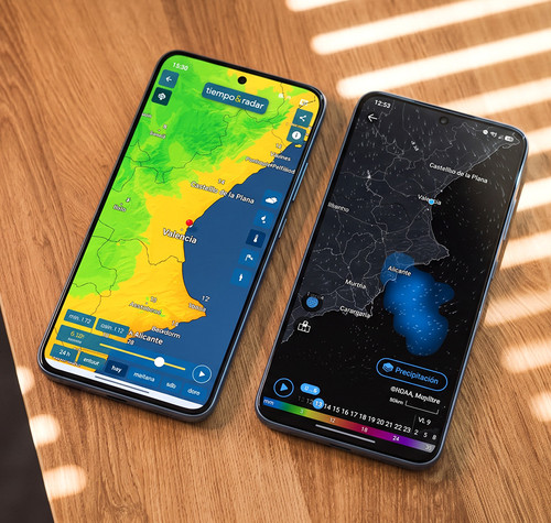 Dos teléfonos móviles sobre una mesa de madera mostrando mapas meteorológicos de la Comunidad Valenciana en sus pantallas.