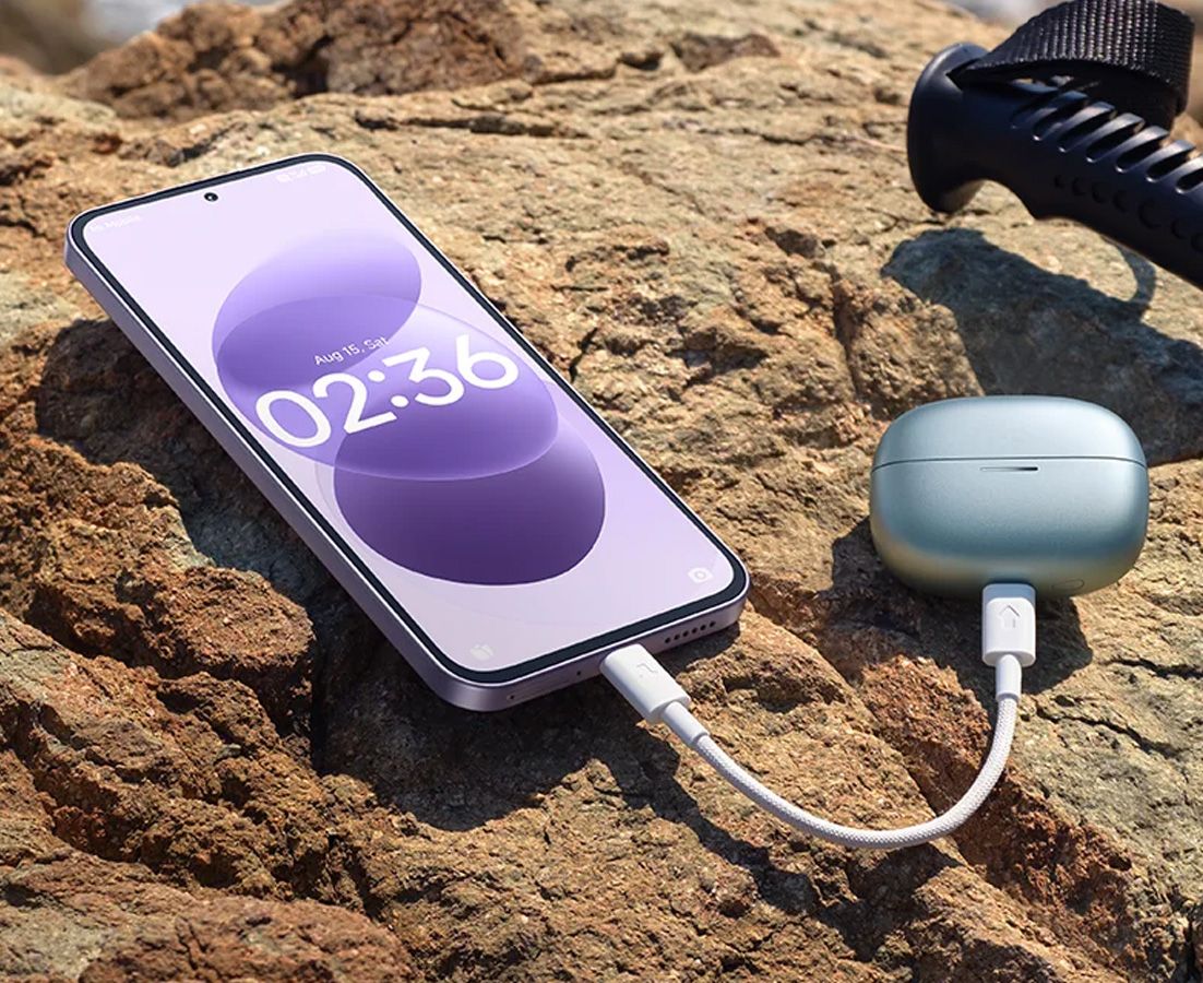 Teléfono Redmi Note 17 5G conectado mediante cable USB-C a un estuche de auriculares inalámbricos sobre una roca.