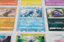 Primer plano de varias cartas de Pokémon coleccionables, incluyendo a Greninja, Cubone y Grimer sobre una superficie blanca.