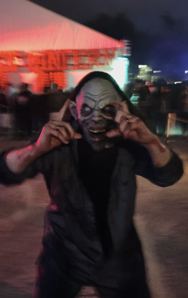 Persona con una máscara de criatura terrorífica gesticulando con las manos hacia su rostro en un evento nocturno.