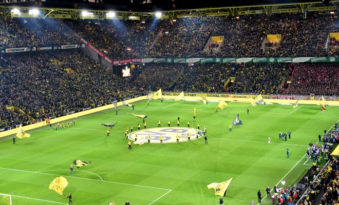 Vista panorámica nocturna de las gradas y el césped del Signal Iduna Park durante la previa de un partido del Borussia Dortmund.