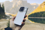 Mano sujetando el teléfono móvil OPPO Find X10 Pro Max en color blanco frente a un lago de montaña y picos rocosos.
