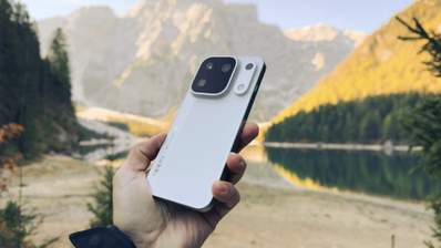 Mano sujetando el teléfono móvil OPPO Find X10 Pro Max en color blanco frente a un lago de montaña y picos rocosos.