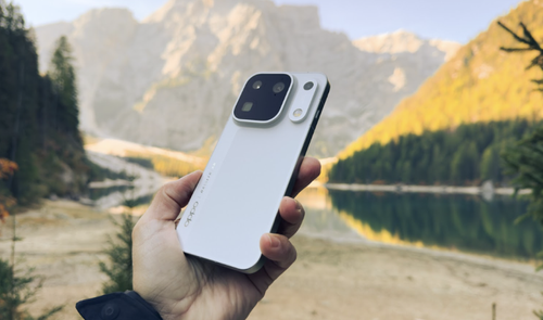 Mano sujetando el teléfono móvil OPPO Find X10 Pro Max en color blanco frente a un lago de montaña y picos rocosos.