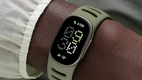 Reloj inteligente Google Fitbit Edge con correa verde oliva en la muñeca, mostrando la hora y datos de actividad física.