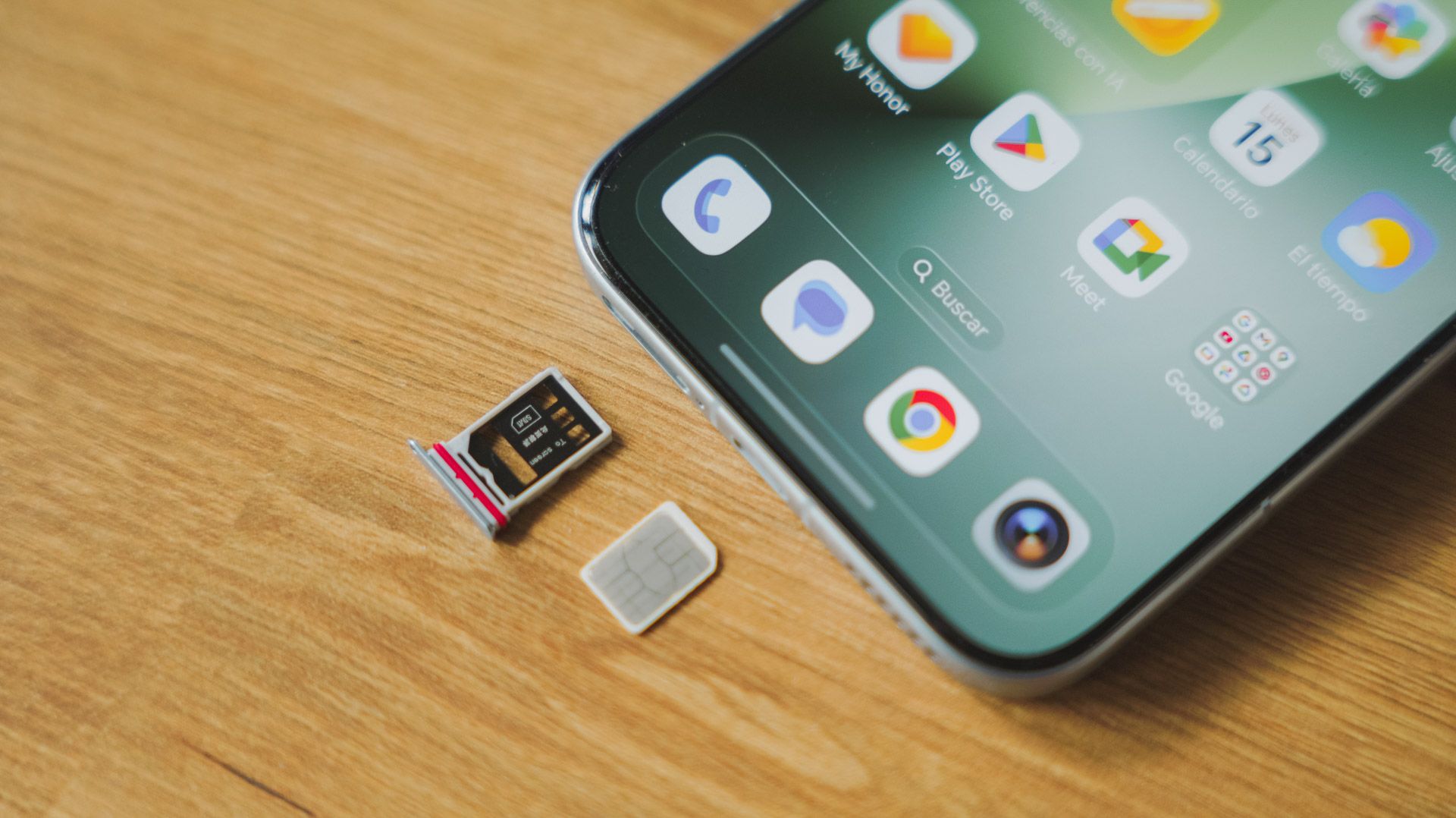 Bandeja de tarjeta nano-SIM extraída junto al borde inferior de un teléfono Honor Magic8 Pro sobre una mesa de madera.
