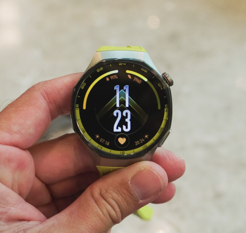 Primer plano de un Huawei Watch GT7 con correa de color verde lima sostenido por una mano.