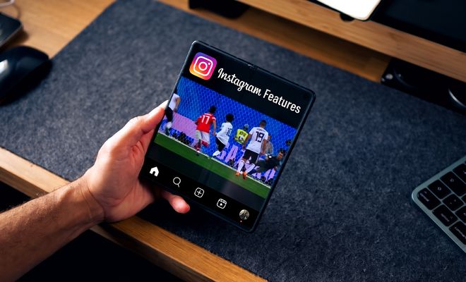 Mano sujetando un teléfono plegable abierto que muestra la interfaz de Instagram sobre un escritorio.