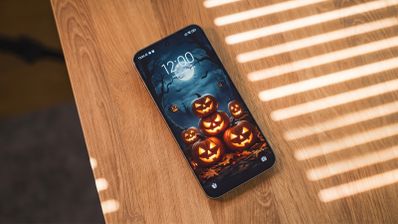 Teléfono móvil sobre una mesa de madera con un fondo de pantalla de calabazas de Halloween iluminadas bajo la luz de la luna.